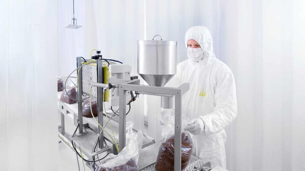 A man in a clean room inoculating mushroom substrate with mycelium at an inoculation machine.
